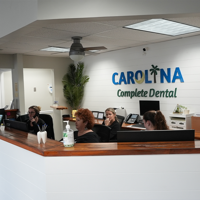 Four Carolina Complete Dental team members sitting behind the front desk