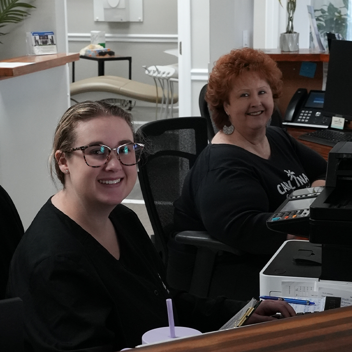 Two smiling dental team members at the front desk