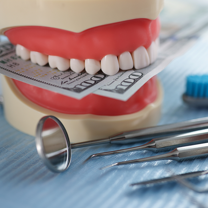 Model of the teeth holding hundred dollar bills next to dental instruments