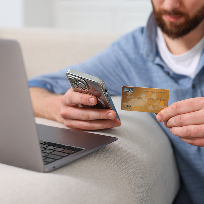 Person entering their payment card information onto a computer while holding their phone