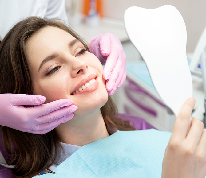 Young woman in the dental chair looking at her smile in a mirror